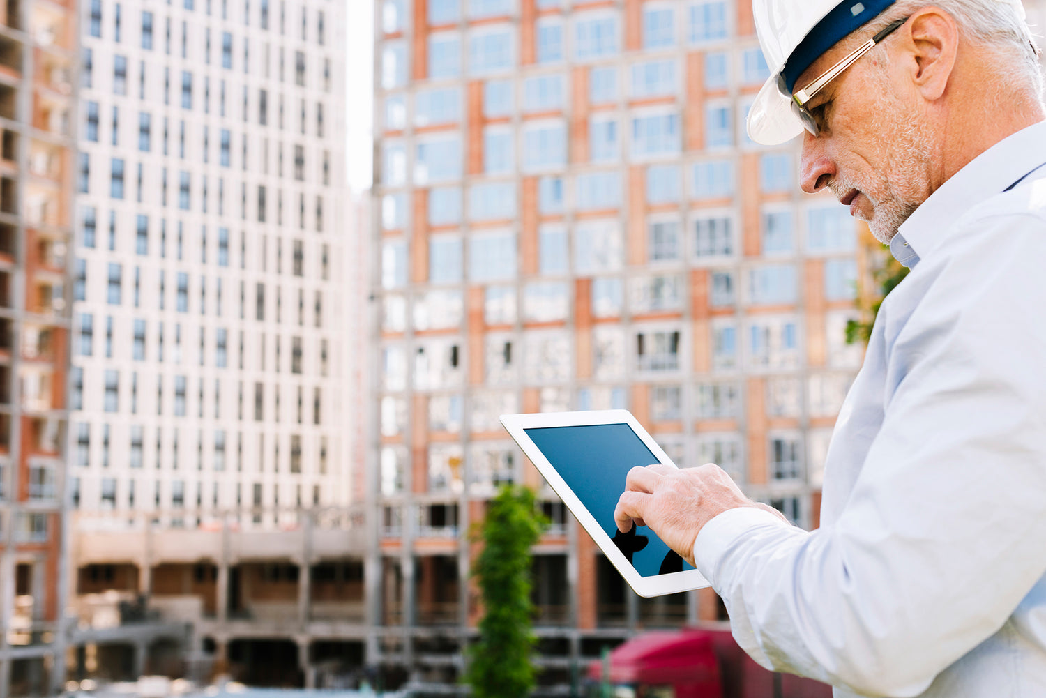 Un termotecnico con casco protettivo sta digitando su un tablet. Sullo sfondo un enorme complesso residenzionale.