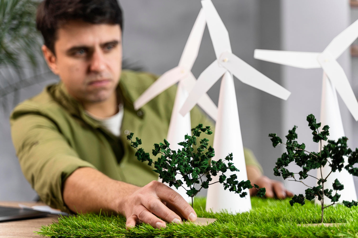 Ingegnere in fase di allestimento di un modellino da tavolo simulante un progetto di turbine eoliche. Erba e alberi finti, turbine eoliche bianche.
