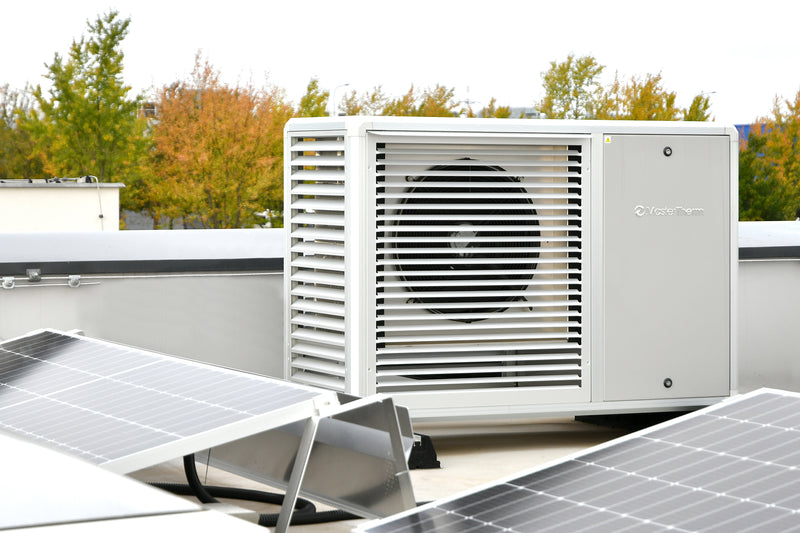 Una pompa di calore installa su un tetto di un'abitazione civile dove sono presenti anche alcuni pannelli solari. Pompa di medie grandi dimensioni con alette e vano compressore. Case bianco dall'ottimo design.